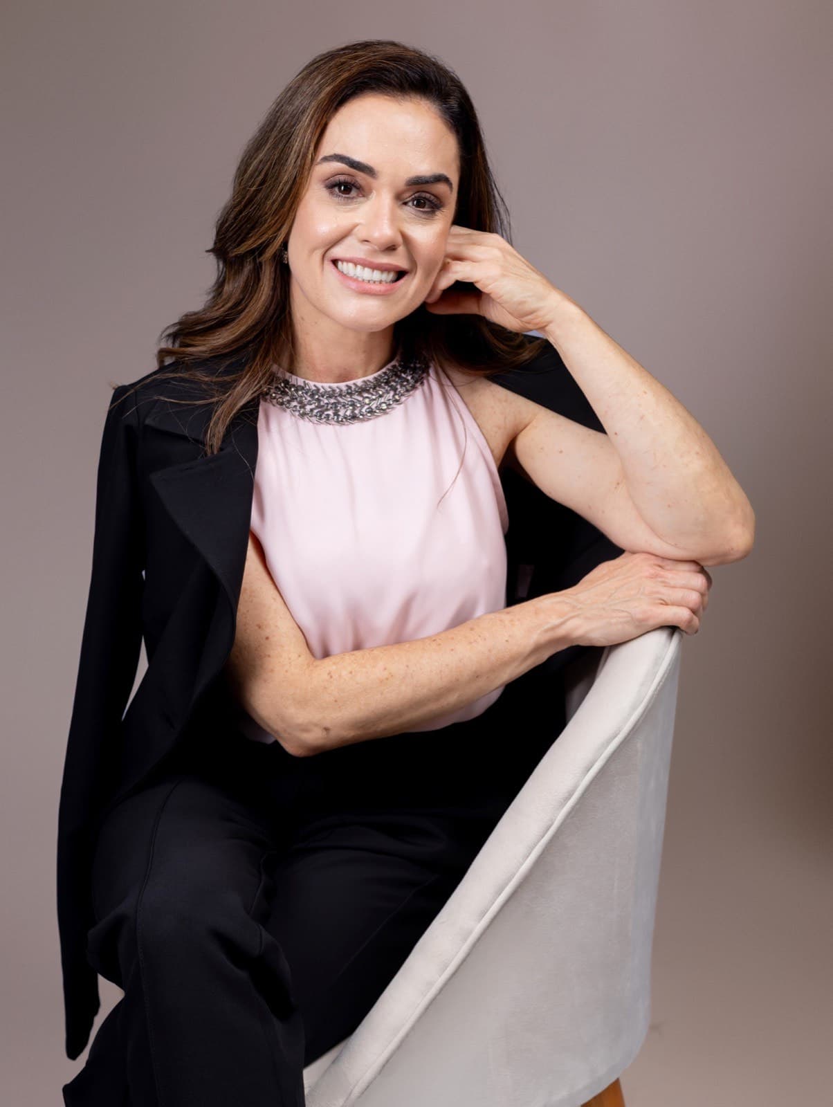 Dra. Lizeta Cristine Lemes Saúde sentada, retrato de corpo inteiro em fundo neutro